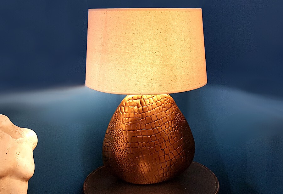 Lampe décorative allumée dans un salon, pied texturé croco, offrant une lumière douce.