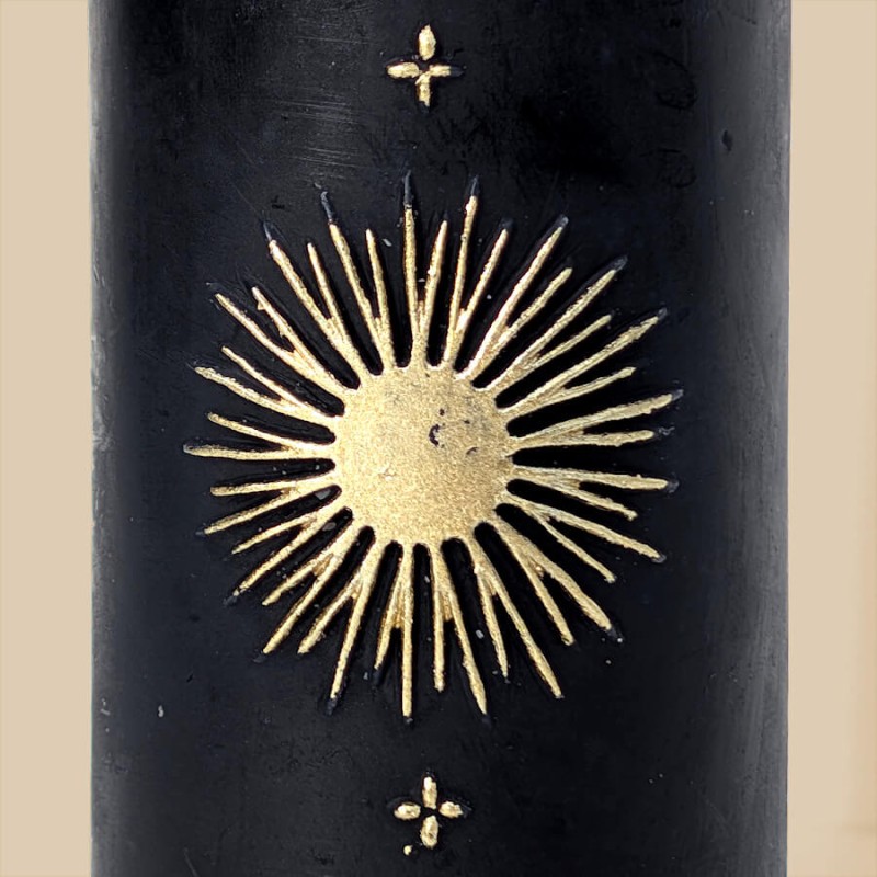 Gros plan sur le motif soleil radieux doré sur la bougie noire mat.