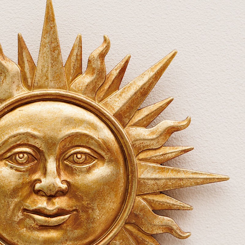 Gros plan sur le visage et les rayons ciselés de la décoration murale Ex-Voto Soleil Doré en résine.