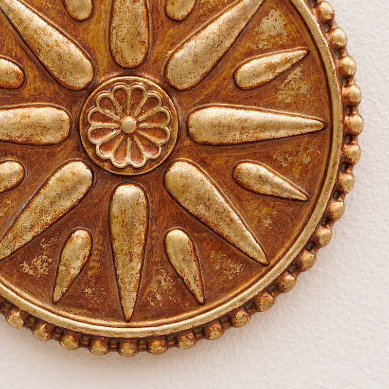 Gros plan sur les rayons et les billes en relief du médaillon Ex-Voto doré (détail texture patinée).