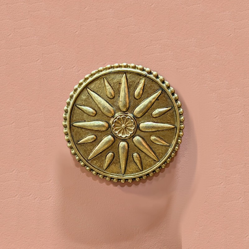 Médaillon Ex-Voto doré (12 cm) en situation, accroché sur un mur de couleur rose poudré (ambiance chaleureuse).