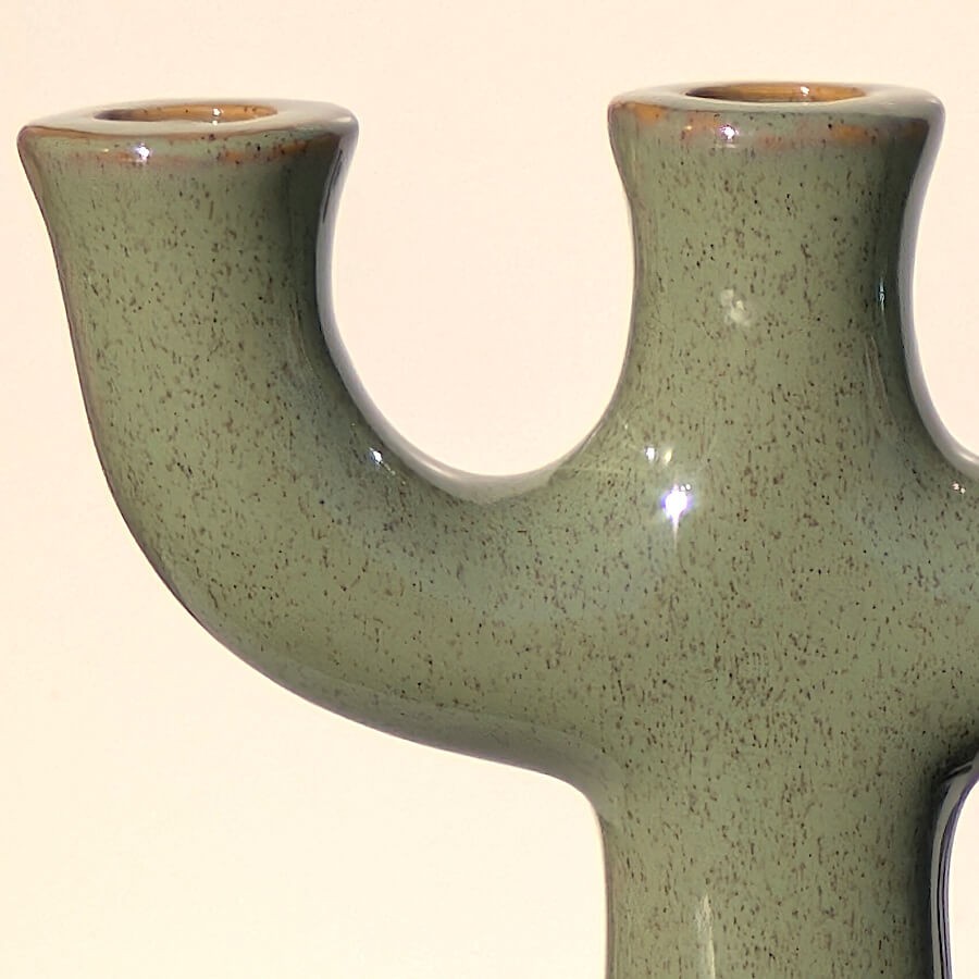 Gros plan sur l'émail vert sauge moucheté et la forme fluide du chandelier.