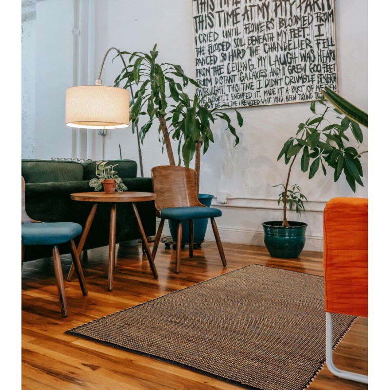 Tapis en jute et coton noir disposé dans un salon contemporain avec plantes.