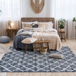 Tapis gris anthracite aux losanges en laine épaisse brute, utilisé en descente de lit pour une ambiance zen et naturelle.