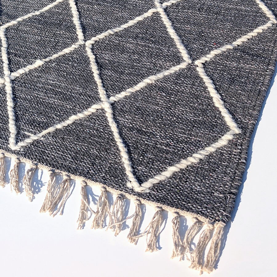 Finition artisanale avec bordure à franges et tissage en laine sur le coton gris anthracite.