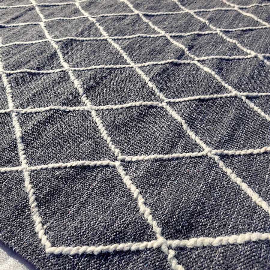 Zoom sur les losanges en laine épaisse créant un relief sculptural contrastant avec le fond en coton gris foncé.