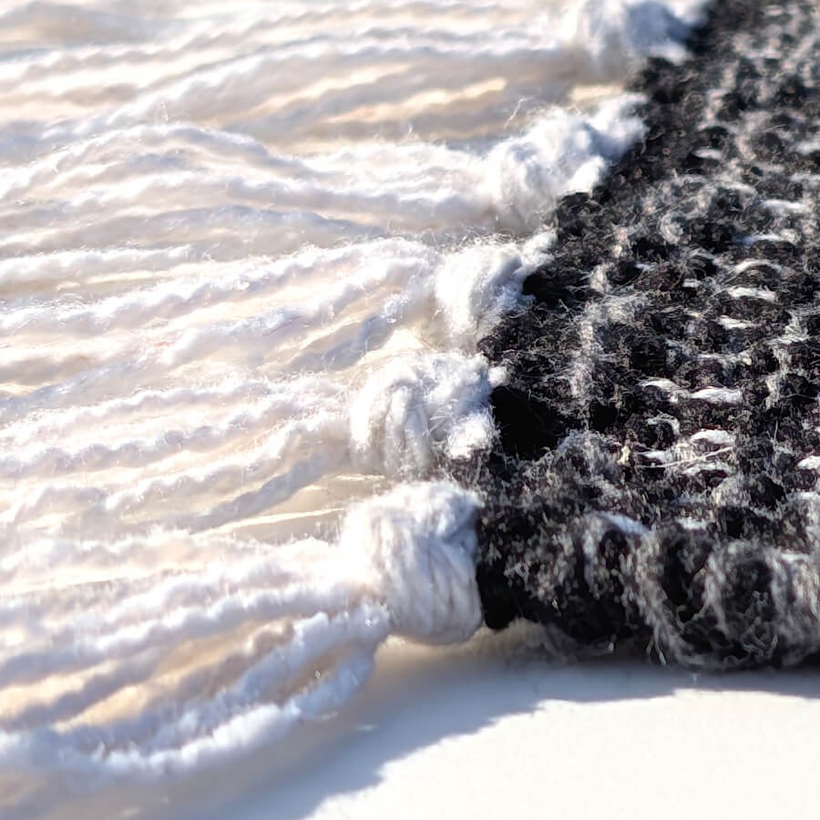 Finitions artisanales du tapis avec franges tressées en coton blanc.