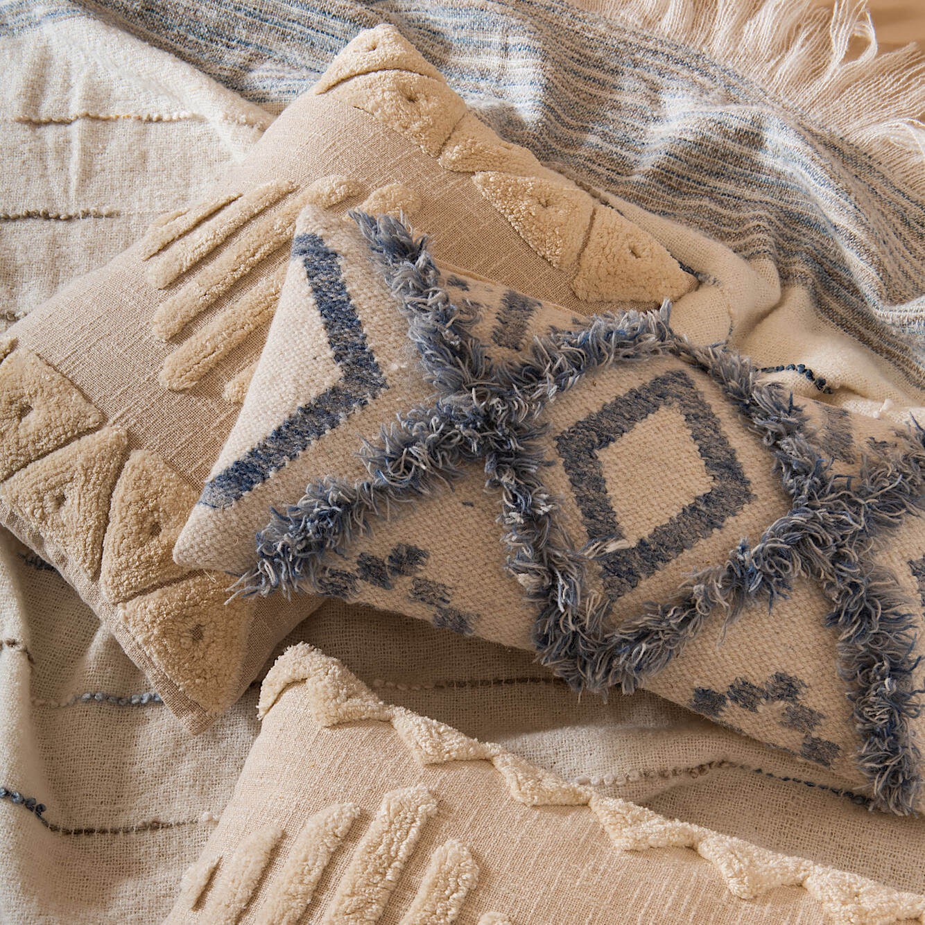 Coussin ethnique bleu et blanc posé sur un plaid beige texturé.