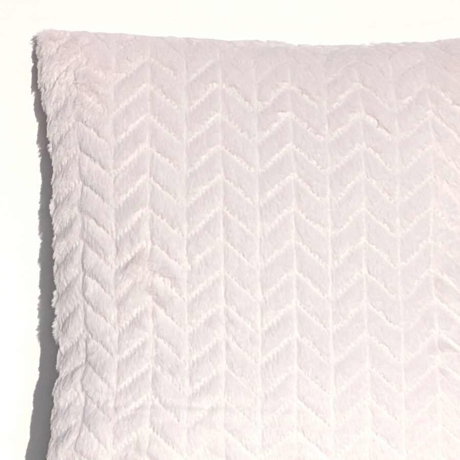 Gros plan sur l'angle du coussin blanc mettant en relief la texture des chevrons et la qualité de la bordure.