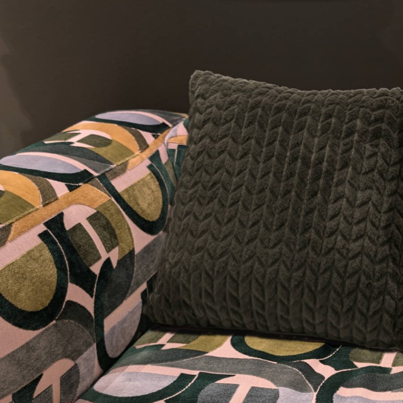 Coussin vert kaki disposé sur un canapé aux motifs graphiques pour une touche de douceur.