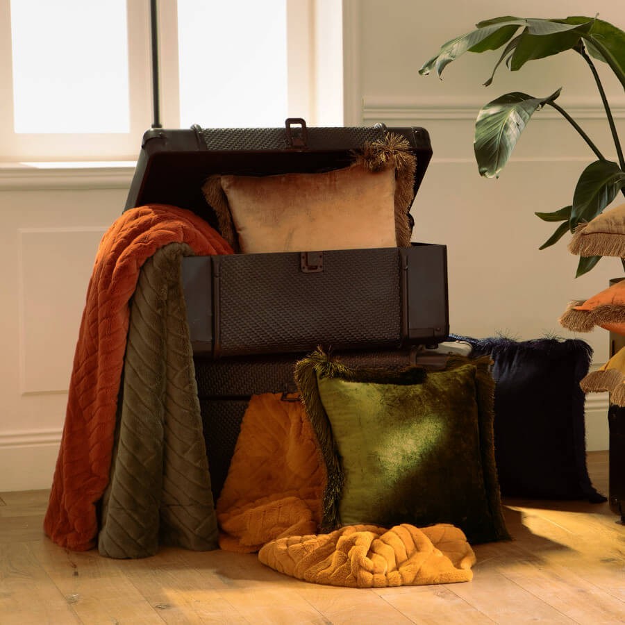 Mise en scène du coussin Kaki et du modèle Camel dans un décor chic avec malle ancienne.