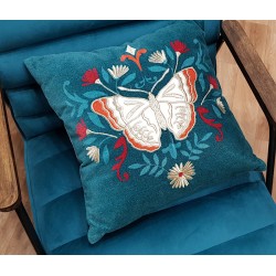 Coussin décoratif papillon bleu canard posé sur un fauteuil en velours bleu.