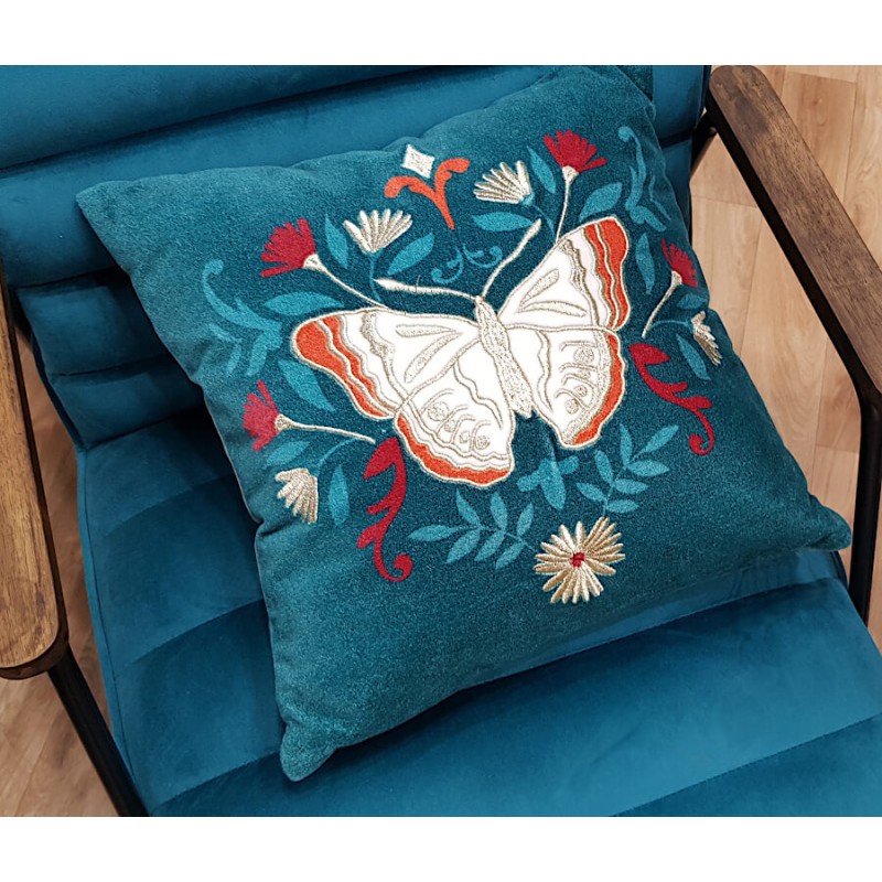 Coussin décoratif papillon bleu canard posé sur un fauteuil en velours bleu.
