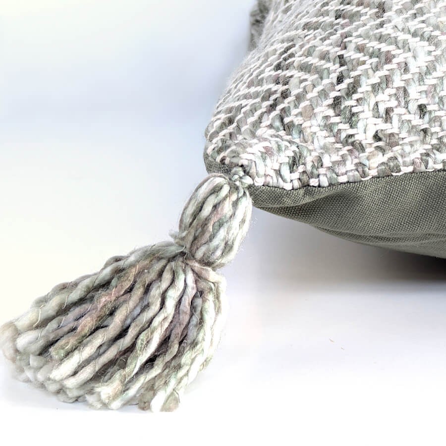 Détail du pompon artisanal bicolore gris et blanc sur l'angle du coussin.