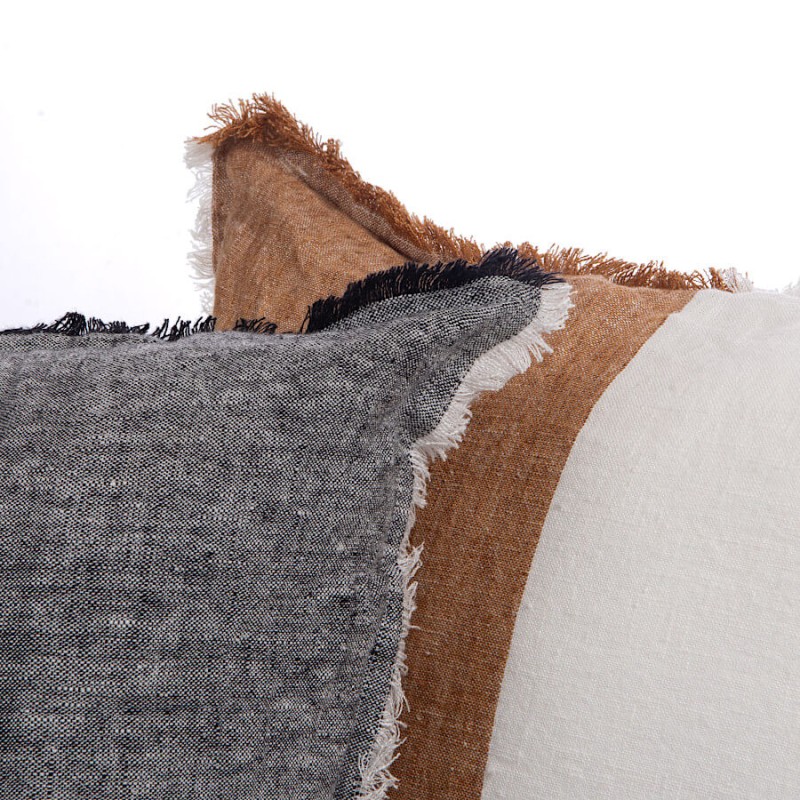 Zoom sur la texture brute des franges et le contraste des couleurs terreuses du coussin 50x50 cm.