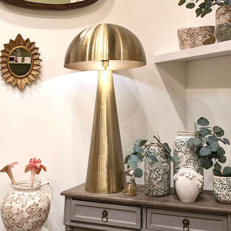 Ambiance lumineuse avec lampe dorée et vase blanc fleuri.