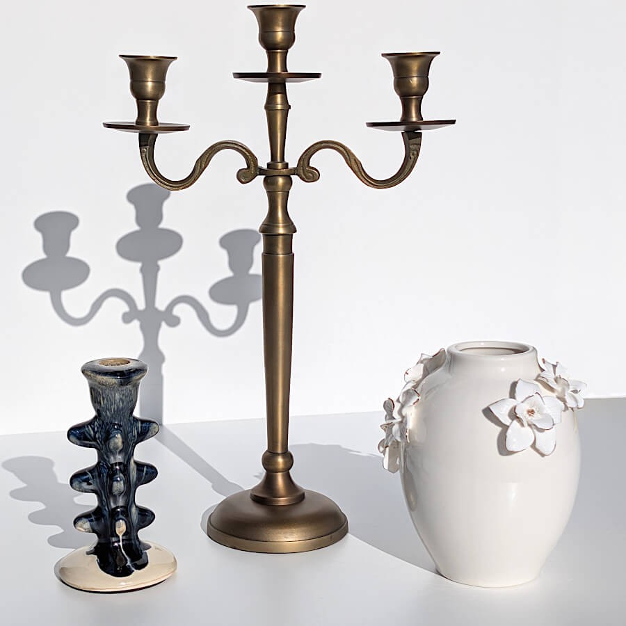 Vase blanc fleuri à côté d'un chandelier en métal doré antique et d'un bougeoir en céramique Deco-Delight.