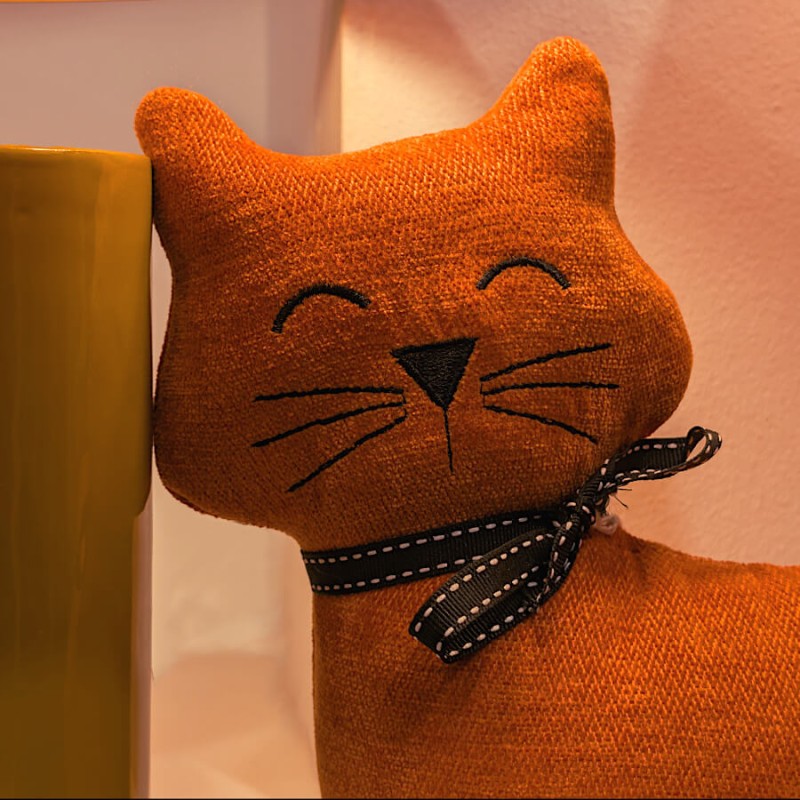 Détail du visage brodé et du ruban noir du chat en tissu.