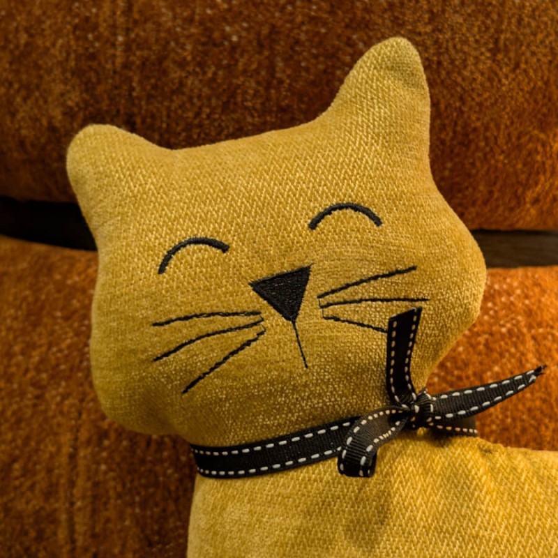 Détail des moustaches et yeux brodés du chat en tissu jaune.