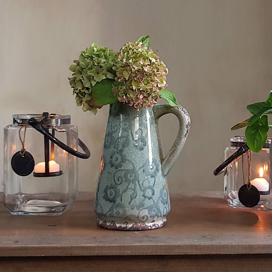 Le pichet décoratif utilisé comme vase avec des hortensias sur un buffet.