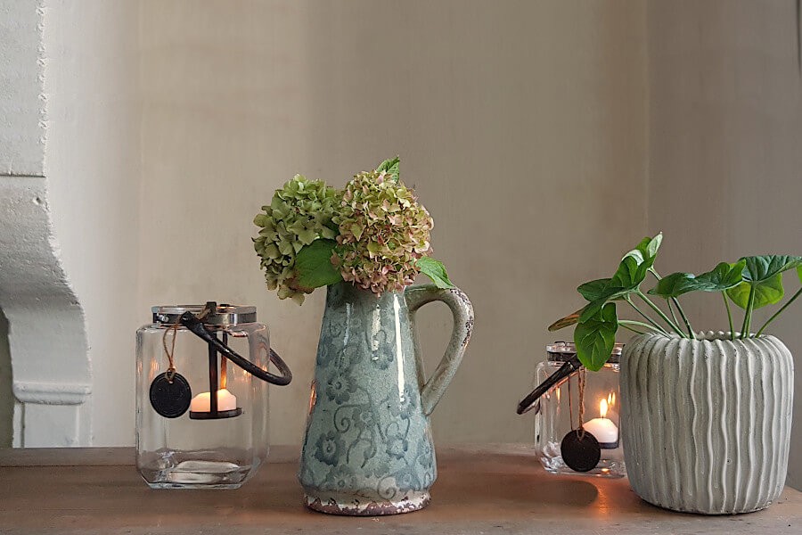Composition déco incluant le pichet, des lanternes et une plante en cache-pot.