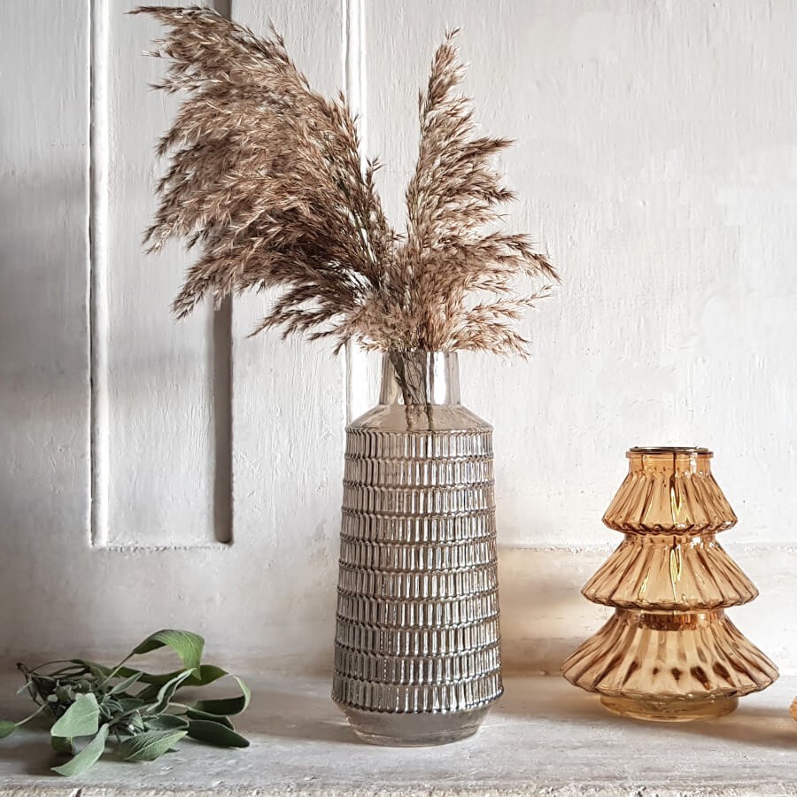 Le vase gris garni d'herbes de la Pampa séchées, près d'un photophore ambré en verre.