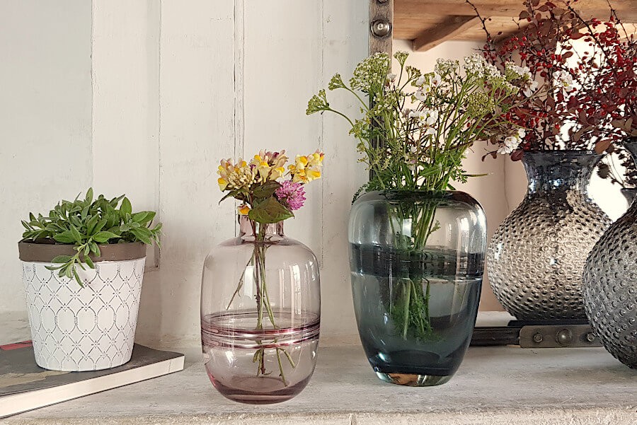 Le vase bleu-gris fleuri à côté du cache-pot blanc et marron, et d'autres vases Deco-Delight, sur une cheminée.