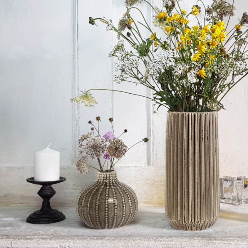 Le vase Origami beige aux côtés du vase texturé "Oursin" et d'une bougie blanche sur un bougeoir en fonte Deco-Delight.
