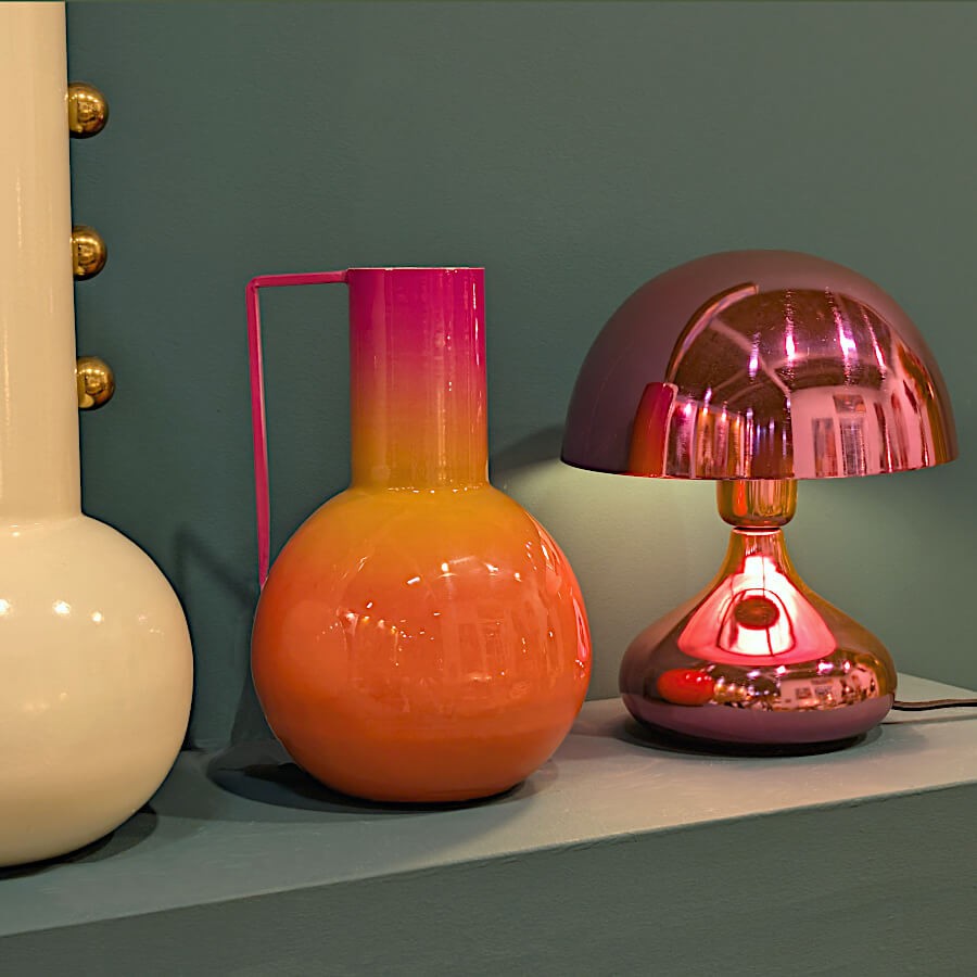 Mise en scène de la lampe à côté du vase orange sur un fond vert pour un contraste Dopamine Decor.