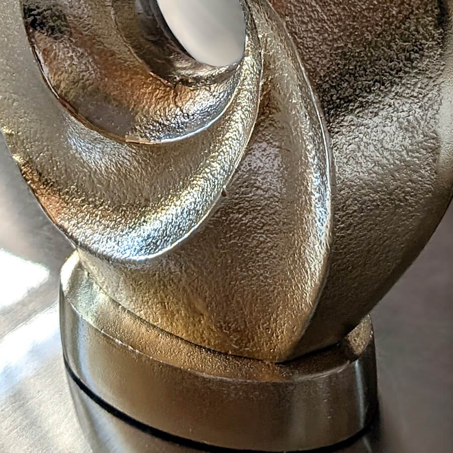 Gros plan sur le socle ovale et la partie inférieure de la structure torsadée pour illustrer sa stabilité et sa finition dorée.