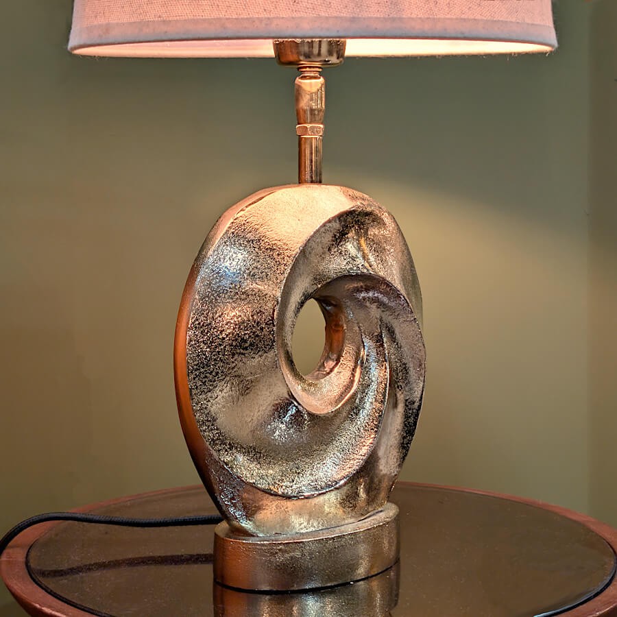 Vue de trois-quarts de la lampe allumée, montrant la profondeur du design sculptural et les reflets du métal sous la lumière.