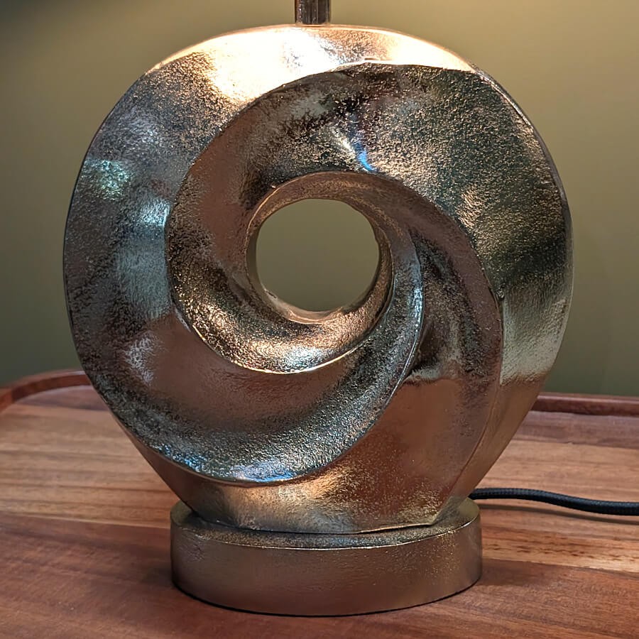 Gros plan de face sur le pied sculptural, révélant le tourbillon central et les reflets métalliques sur le socle rond.