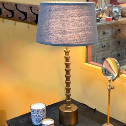 Mise en situation de la lampe Totem allumée diffusant une lumière chaleureuse sur un meuble en bois.