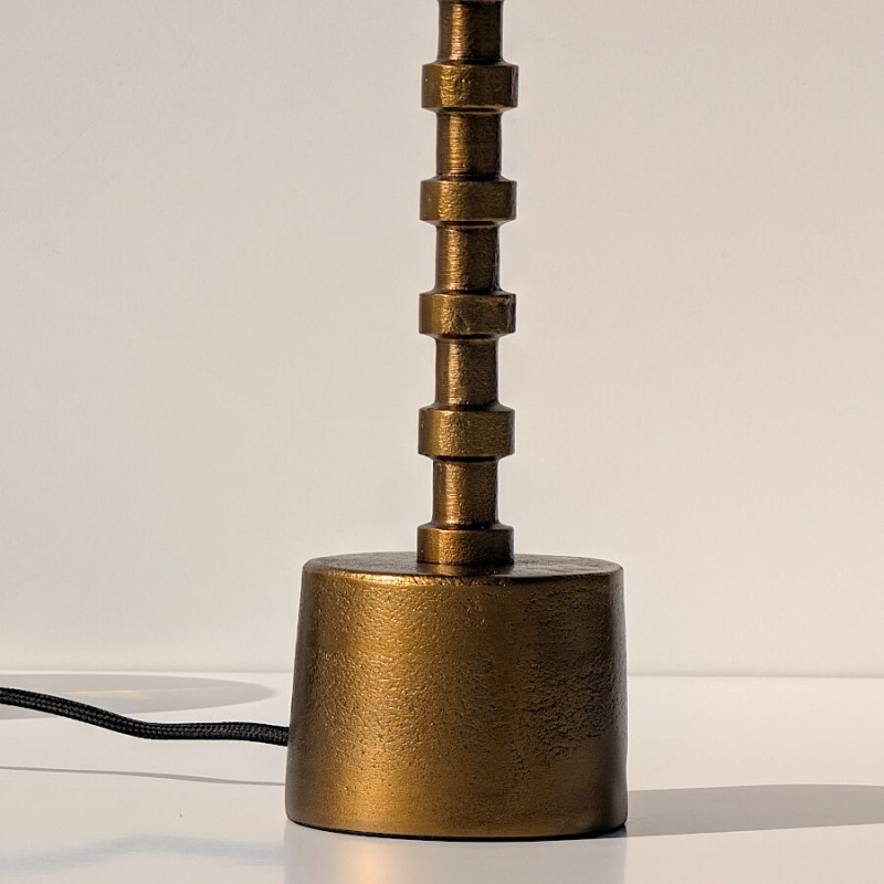 Zoom sur la base cylindrique en métal doré brossé et le détail des anneaux du pied.