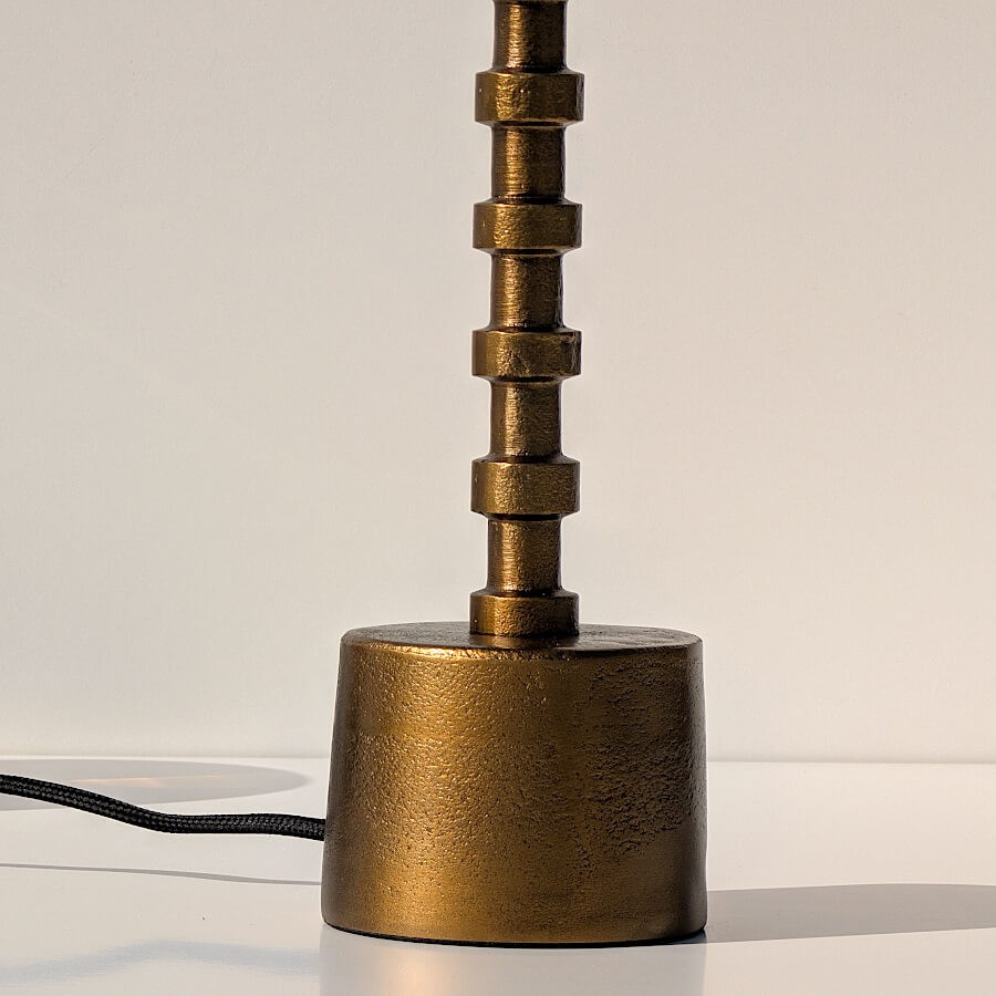 Zoom sur la base cylindrique en métal doré brossé et le détail des anneaux du pied.