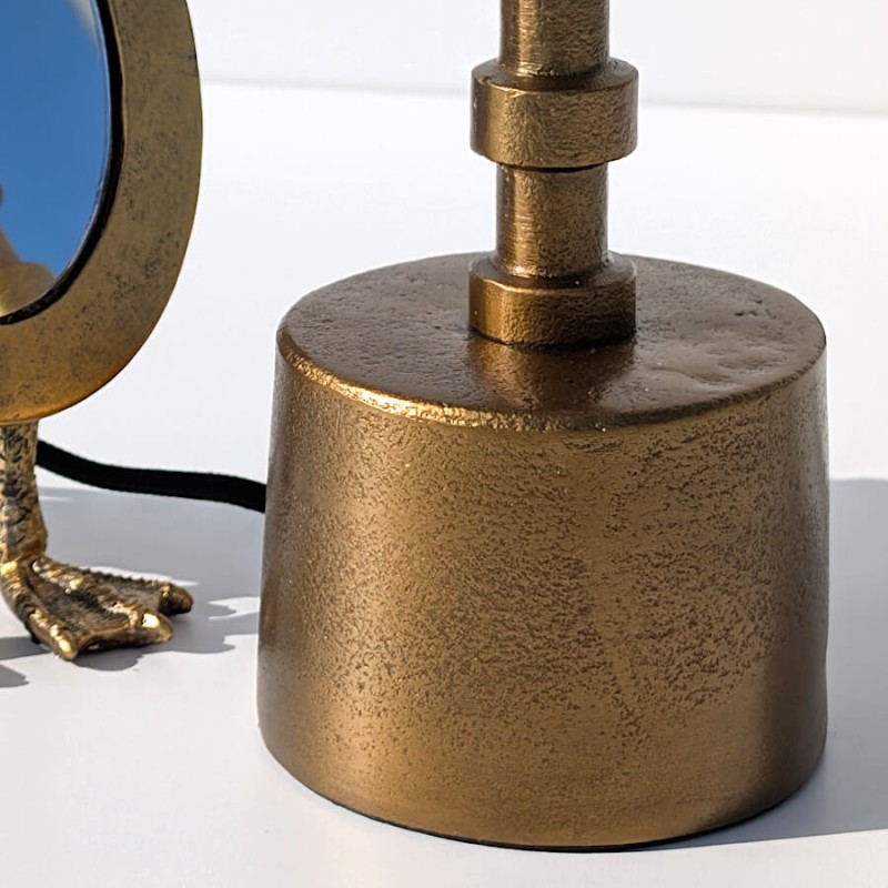 Gros plan sur la finition artisanale du socle en métal doré et le départ de la tige annelée.