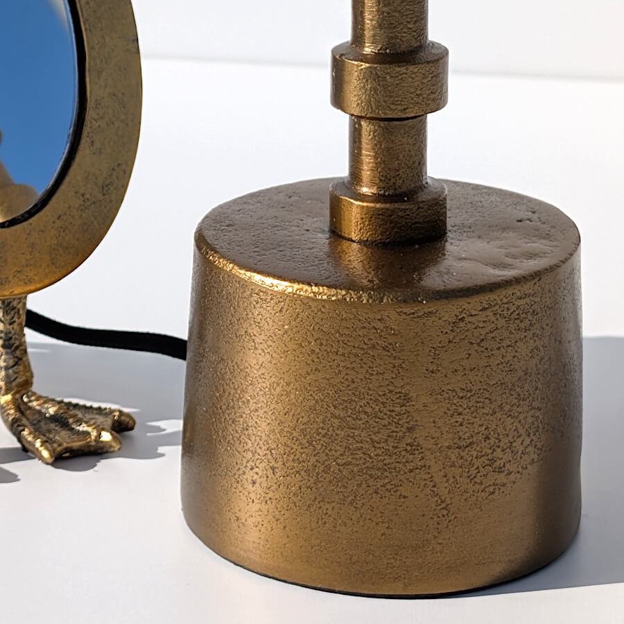 Gros plan sur la finition artisanale du socle en métal doré et le départ de la tige annelée.