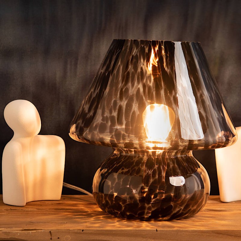 Lampe en verre moucheté éclairée créant une ambiance douce et chaleureuse sur bois.