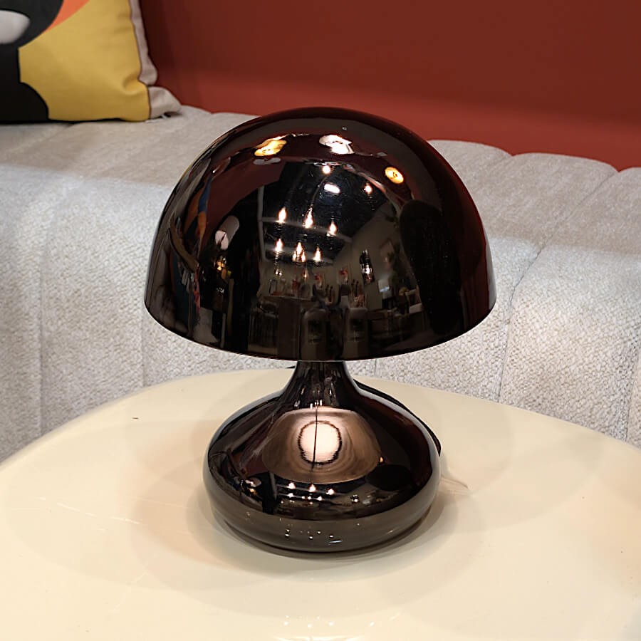 Lampe champignon noire éclairée sur une table d'appoint, ambiance feutrée.