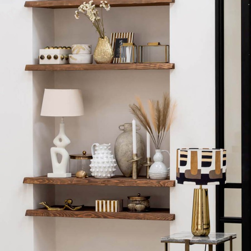 La lampe graphique présentée dans une niche décorative avec des objets en céramique blanche et dorée.