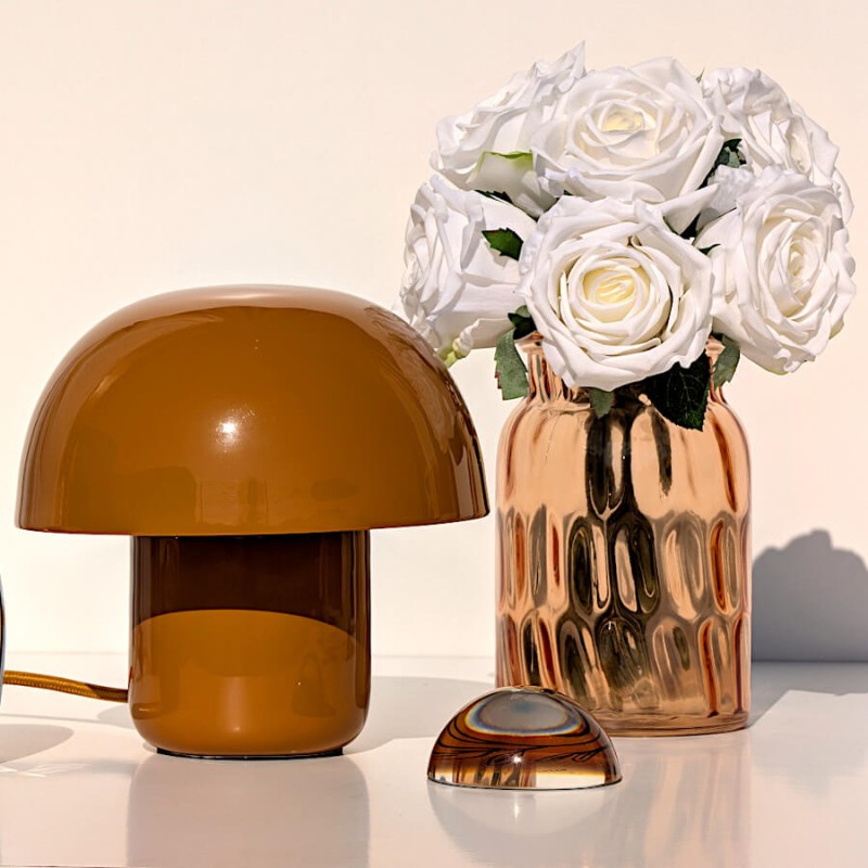 Mise en scène complète : lampe, roses, vase brun et presse-papier en verre ambré.