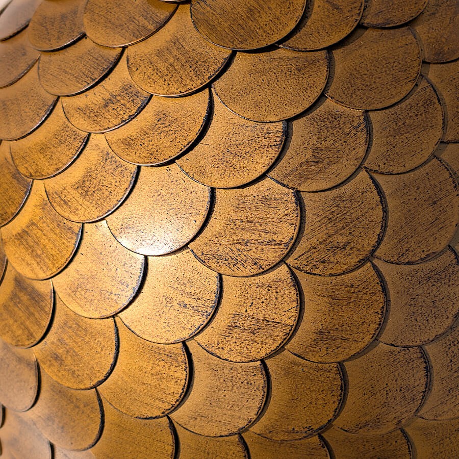 Focus macro sur le motif des écailles et la patine dorée travaillée.