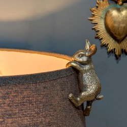 Le petit lapin malicieux en équilibre sur le bord d'un abat-jour gris.