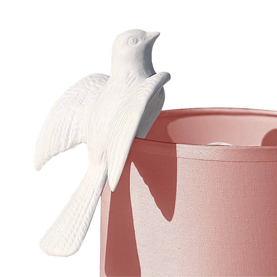 Figurine colombe en céramique biscuit immaculée, posée sur un abat-jour rose.