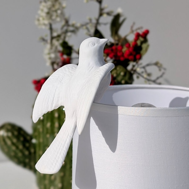 Détail de la colombe surplombant un abat-jour avec des fleurs séchées dans le vase cactus en fond.