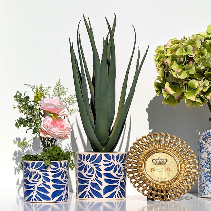 Scène déco avec cadre doré, plantes vertes et fleurs roses.