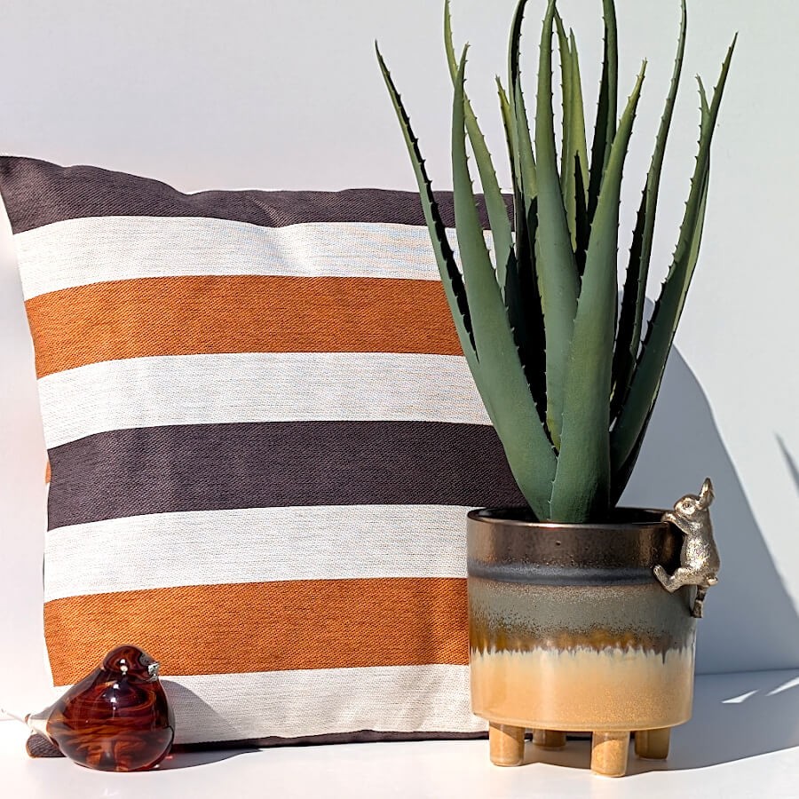 Ambiance cosy avec le coussin caramel rayé et accessoires terre cuite de la collection Deco-Delight.