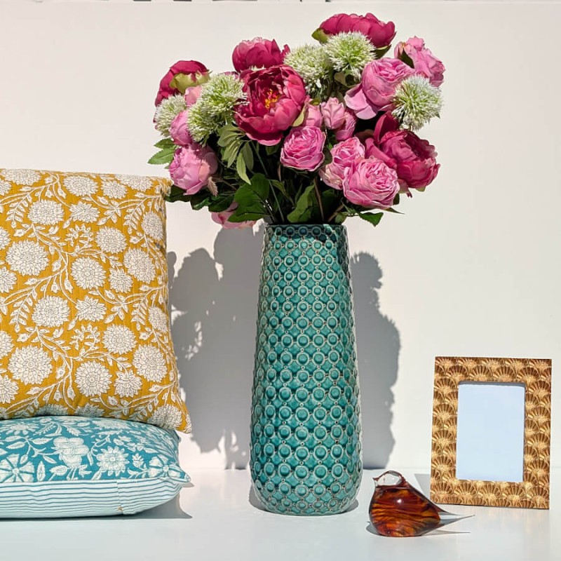 Composition complète avec vase turquoise, coussins colorés, cadre photo et statuette.