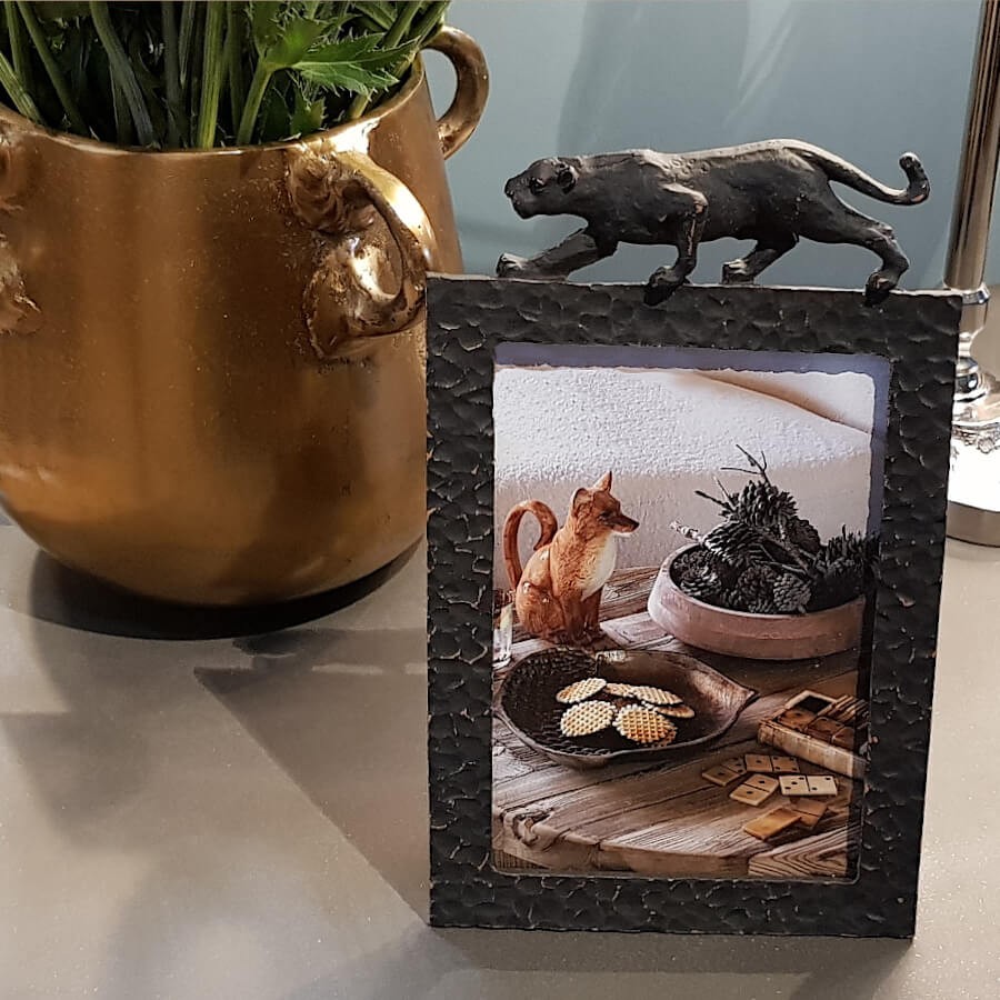 Détail de la panthère surplombant un pot doré texturé.