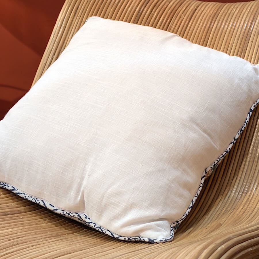 Vue du revers du coussin, montrant la face unie crème en coton.